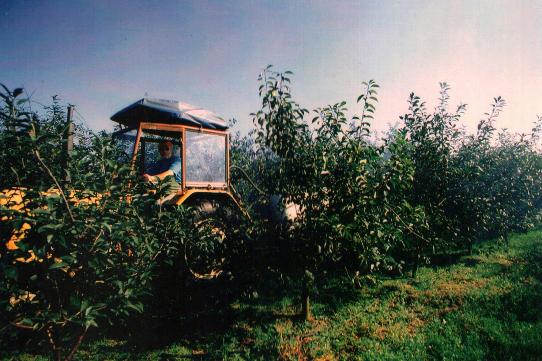 Właściciel sadu i lotniska, Zbigniew Kowalski, osobiście obsługuje ciągnik rolniczy w trakcie opryskiwania drzewek owocowych.