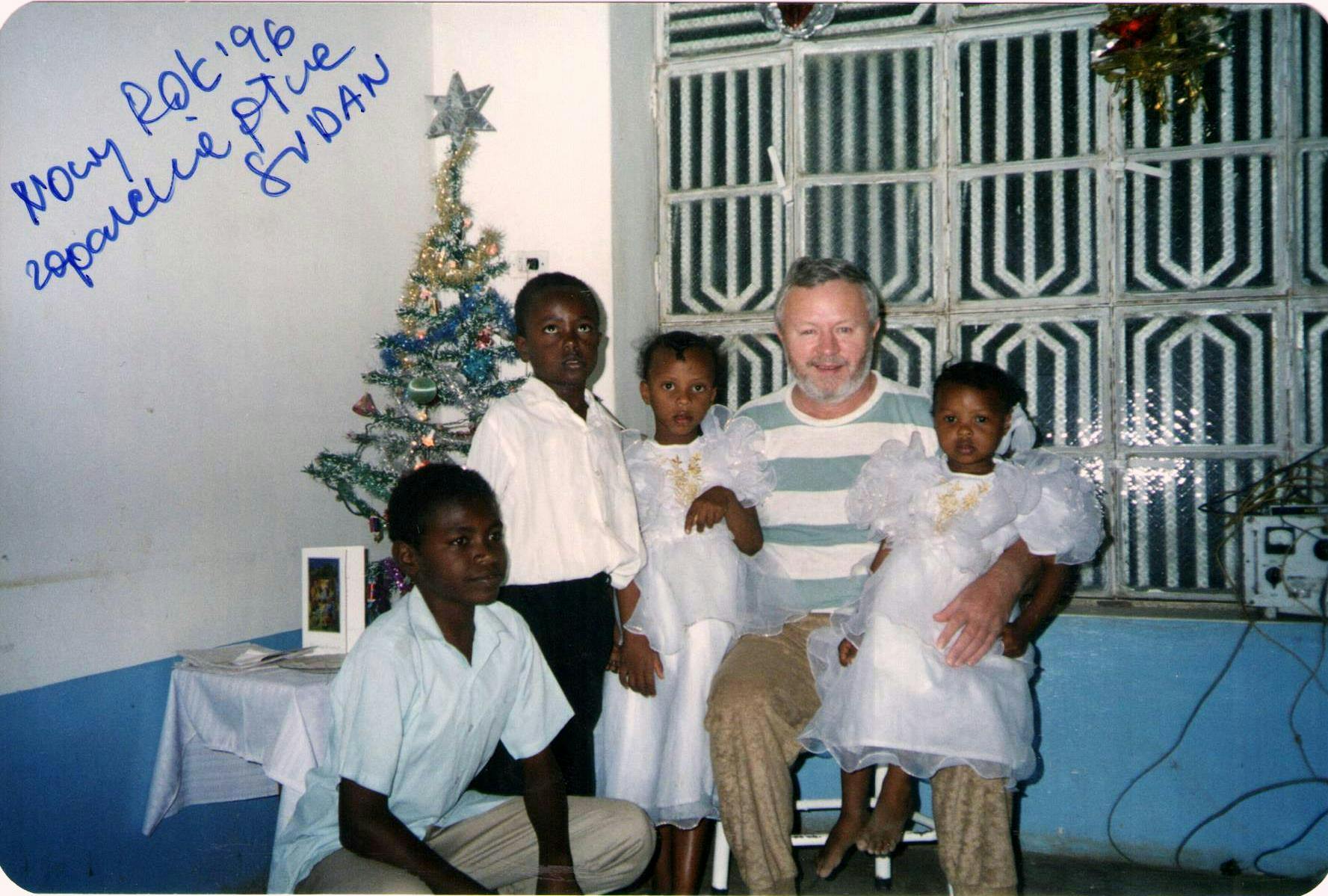 Sudan, lata 90-te XX wieku. Zbigniew Kowalski wśród sudańskich dzieci. W tle bożonarodzeniowa choinka.