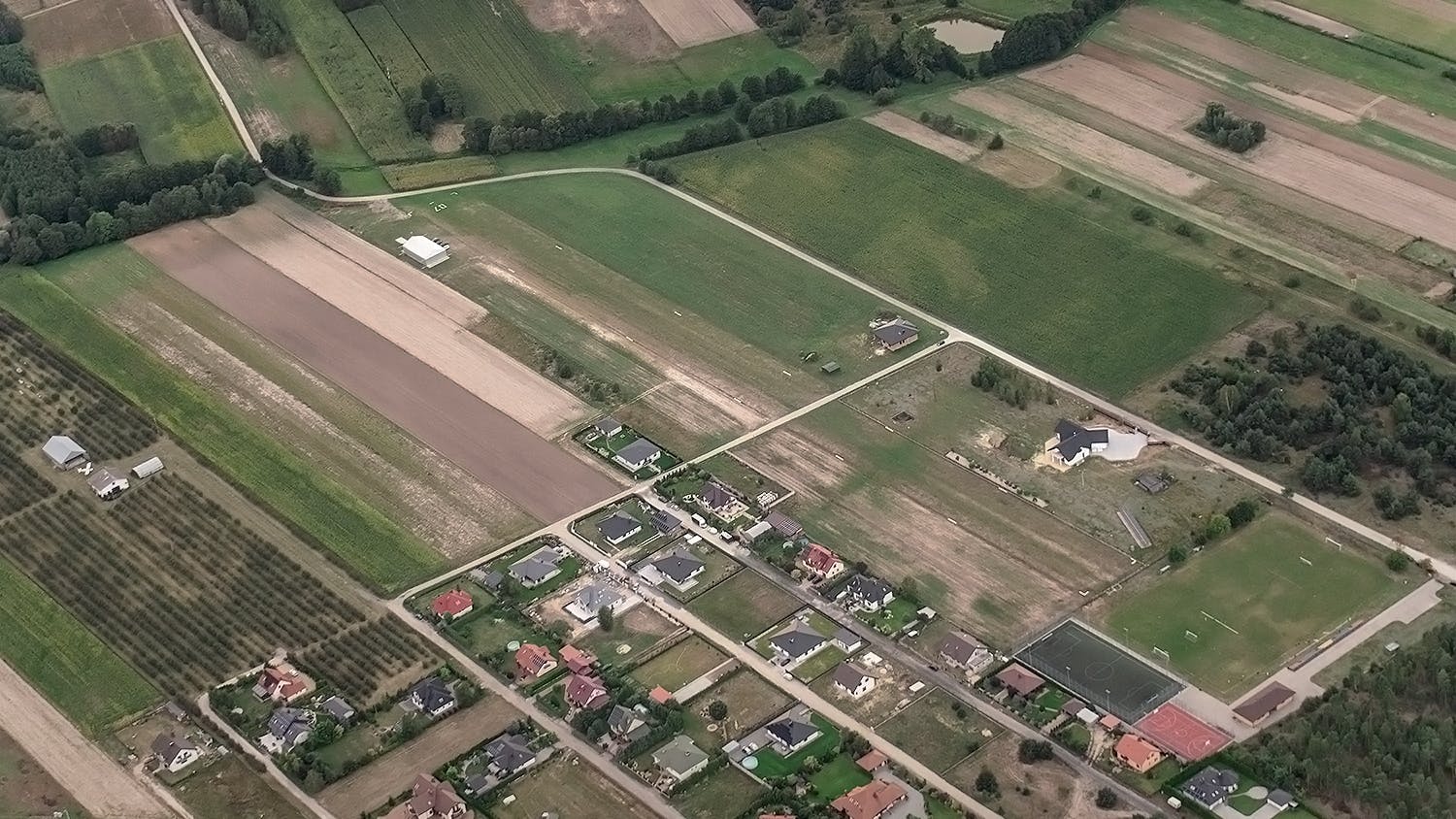 Chojne, 2022 rok. Widok lądowiska z lotu ptaka. Po lewej widoczny dotychczasowy hangar i sad wiśniowy. Na środku pas startowy i nowy hangar.